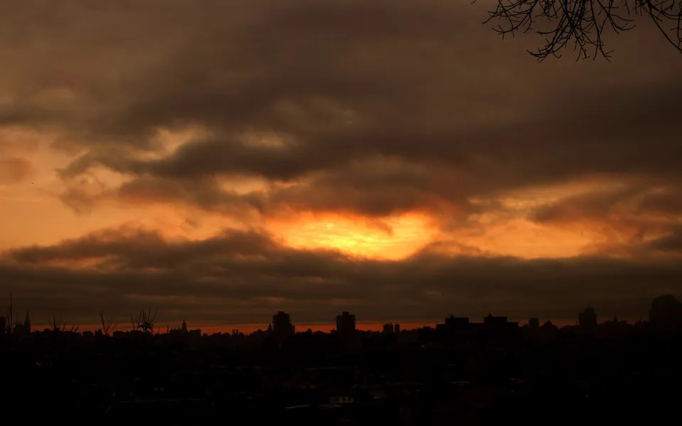 A dramatic sunset with fiery orange clouds illuminating the sky above a dark city skyline.