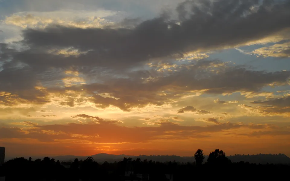A dramatic sunset with golden and orange clouds over a dark, silhouetted landscape.