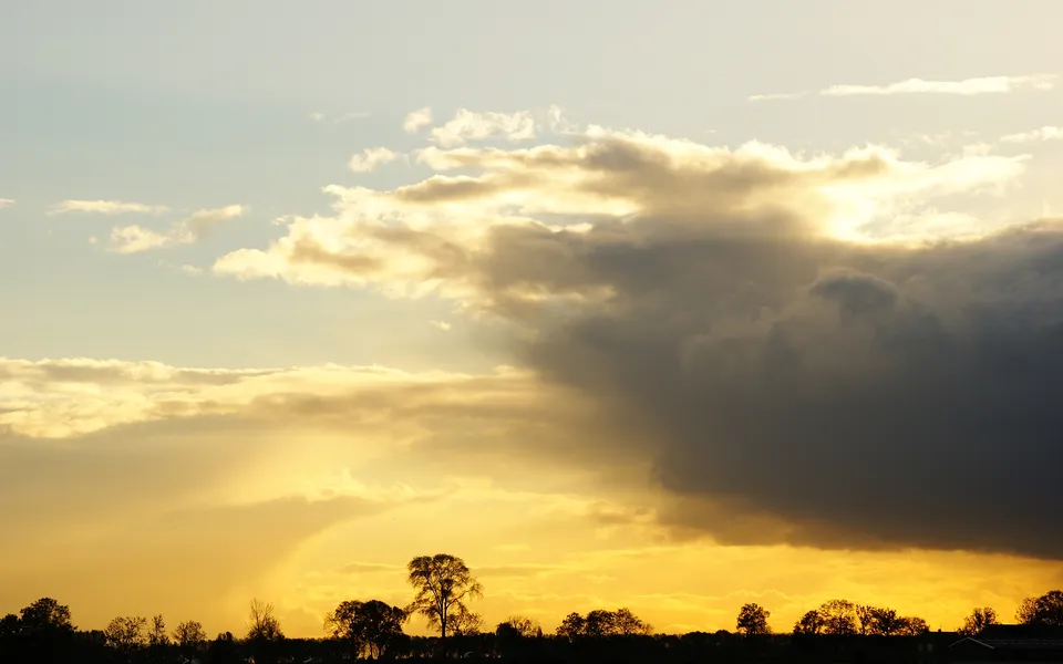 A dramatic sunset sky with golden light breaking through dark clouds, silhouetting trees below.