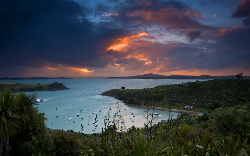 A wide shot of a harbor filled with boats during a dramatic sunset with colorful clouds.