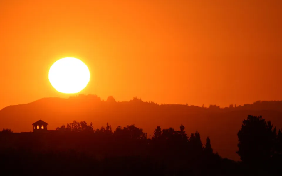A bright, large sun sets behind rolling hills, casting an orange glow over the landscape.