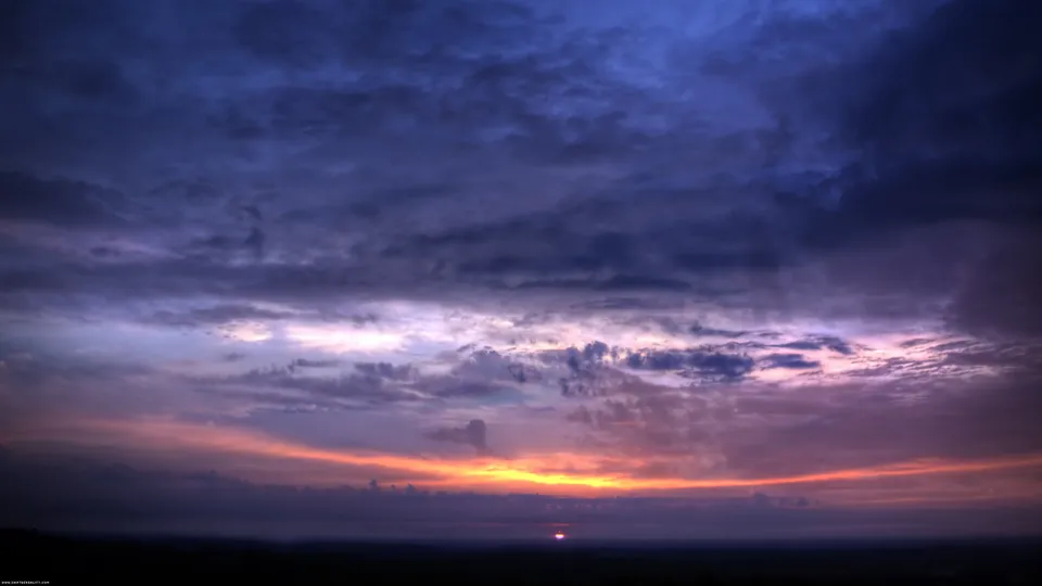 A dramatic sunset with vibrant orange and pink hues illuminating dark, textured clouds.