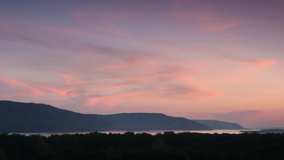 A serene sunset with pink and purple clouds over dark mountains and a calm body of water.