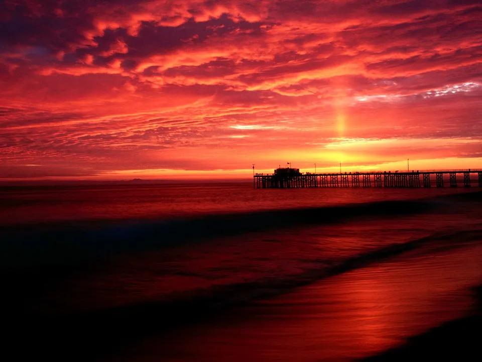 A vibrant red and orange sunset over the ocean with a silhouetted pier.