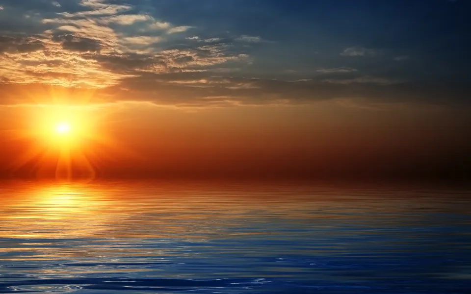 A bright sun with rays shines on the left side of the frame, reflecting on the water below during a sunset.