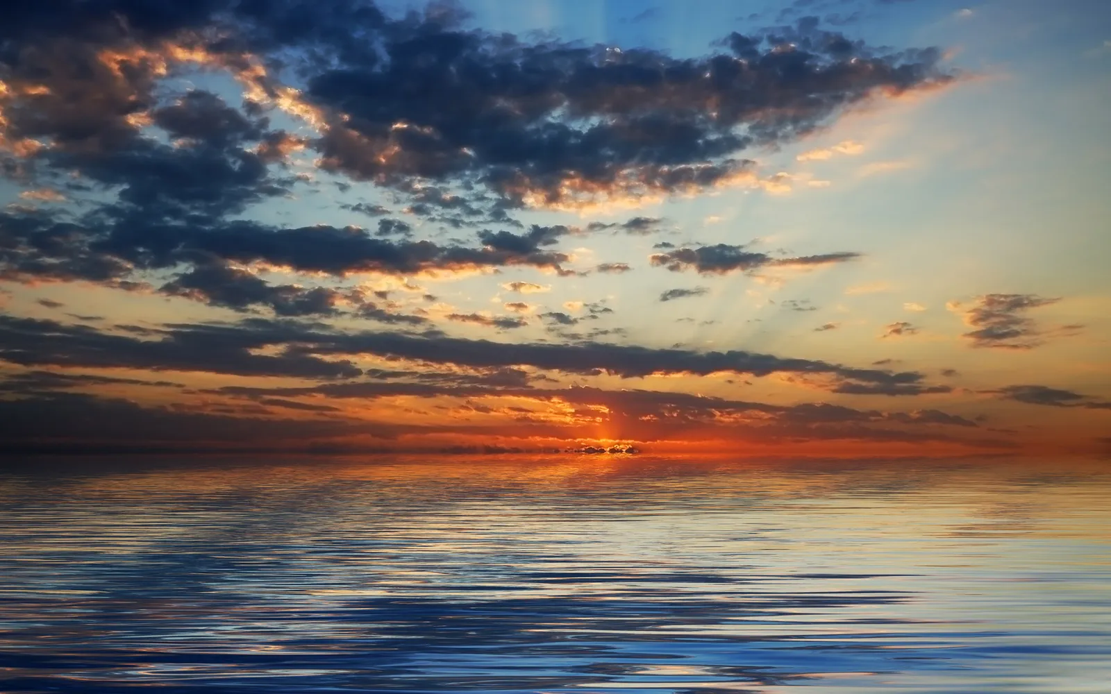 A vibrant sunset with orange and blue clouds reflected in calm water.