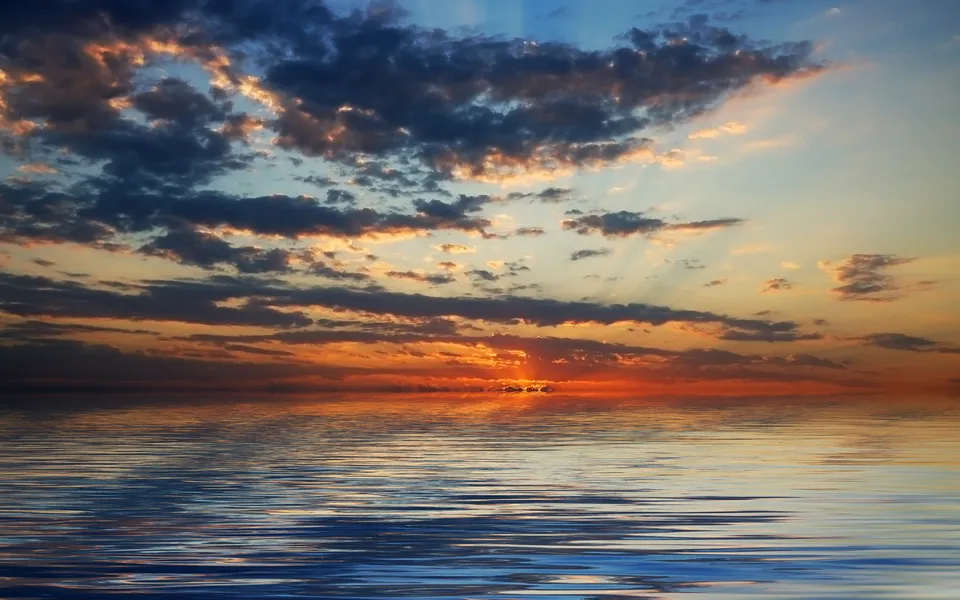 A vibrant sunset with orange and blue clouds reflected in calm water.
