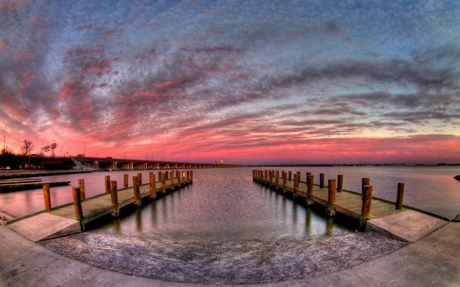 Two wooden docks extend into calm water under a dramatic sky filled with pink and blue clouds at sunset.