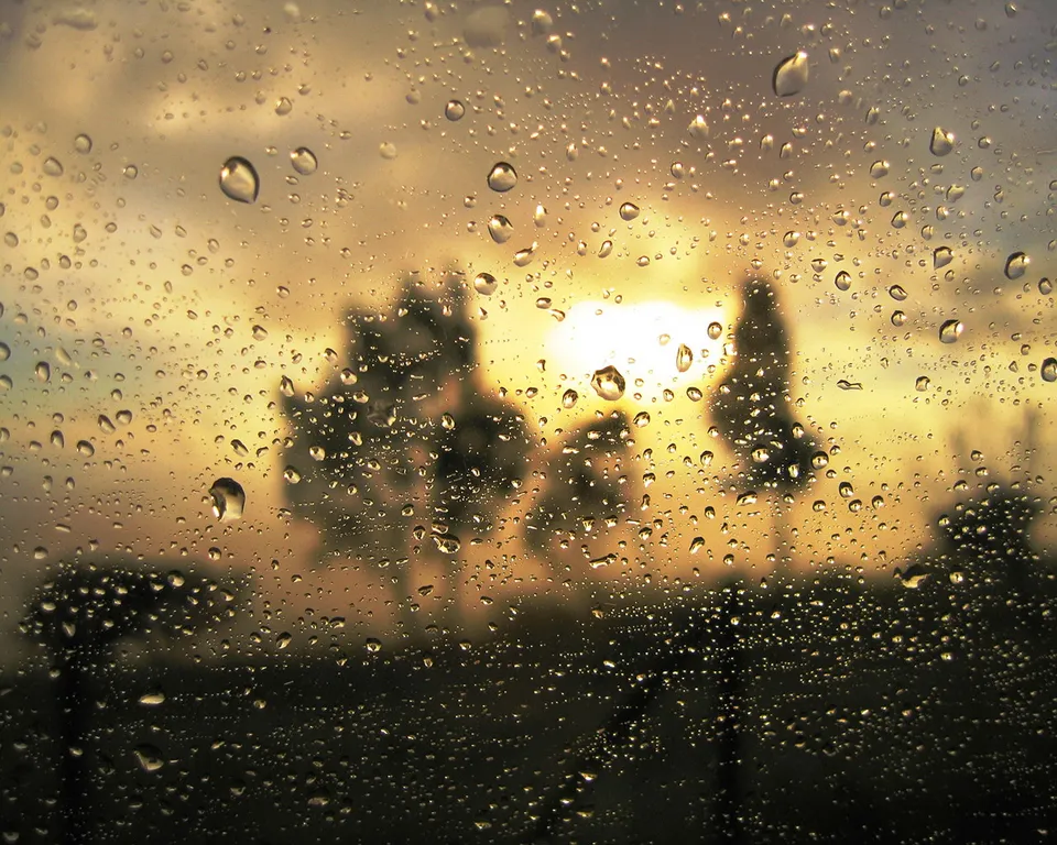 View of a golden sunset through a window covered in raindrops.