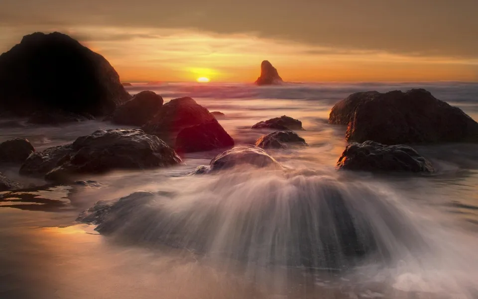 A serene sunset over a rocky coastline with waves gently flowing around the stones.