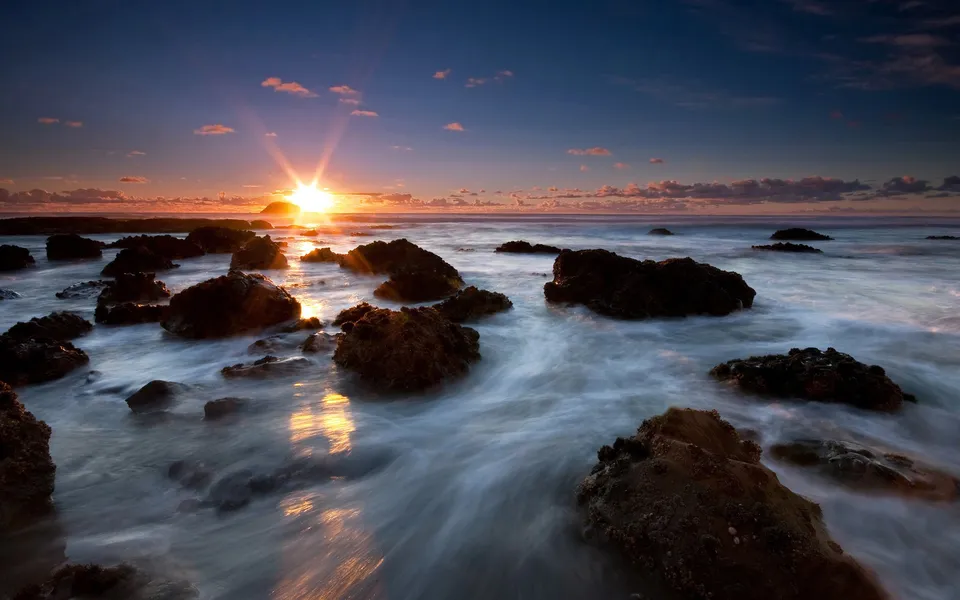 A vibrant sunset over a rocky shoreline with waves gently washing over the rocks.