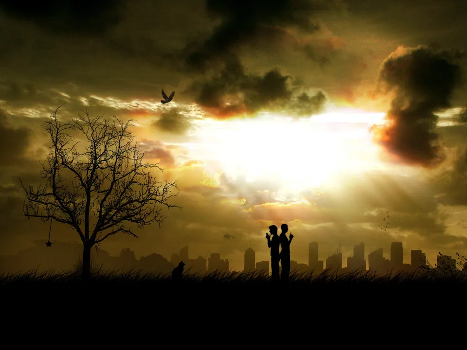 Silhouettes of two people and a tree against a dramatic sunset sky with city skyline in the background.