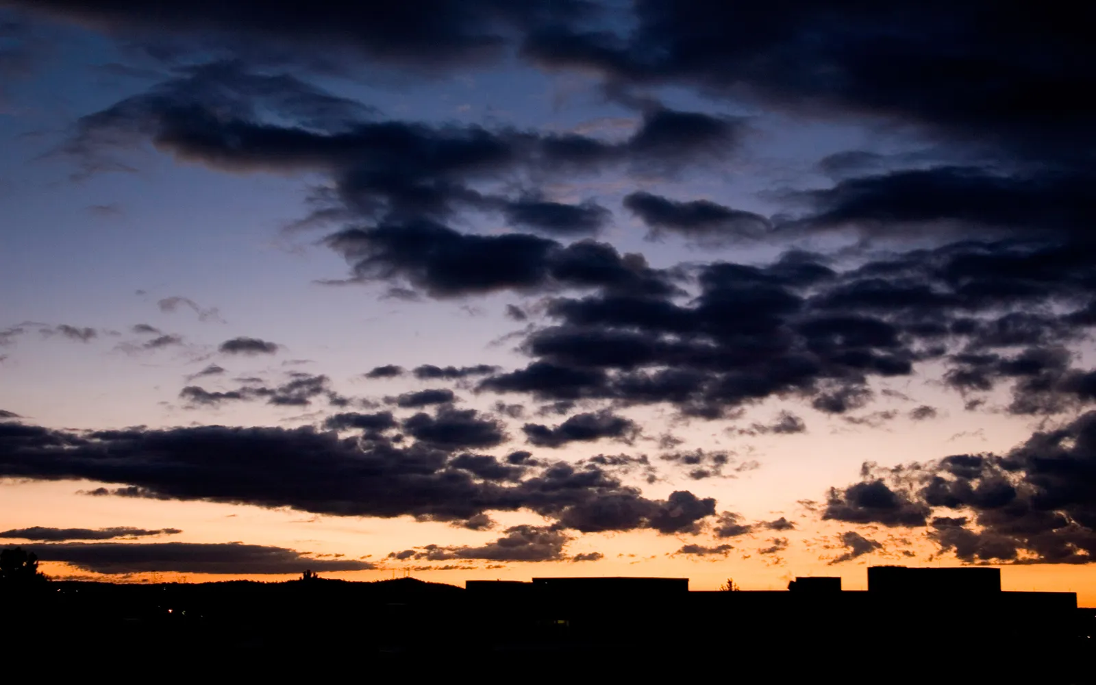Dark clouds fill the sky above a silhouetted landscape at sunset.