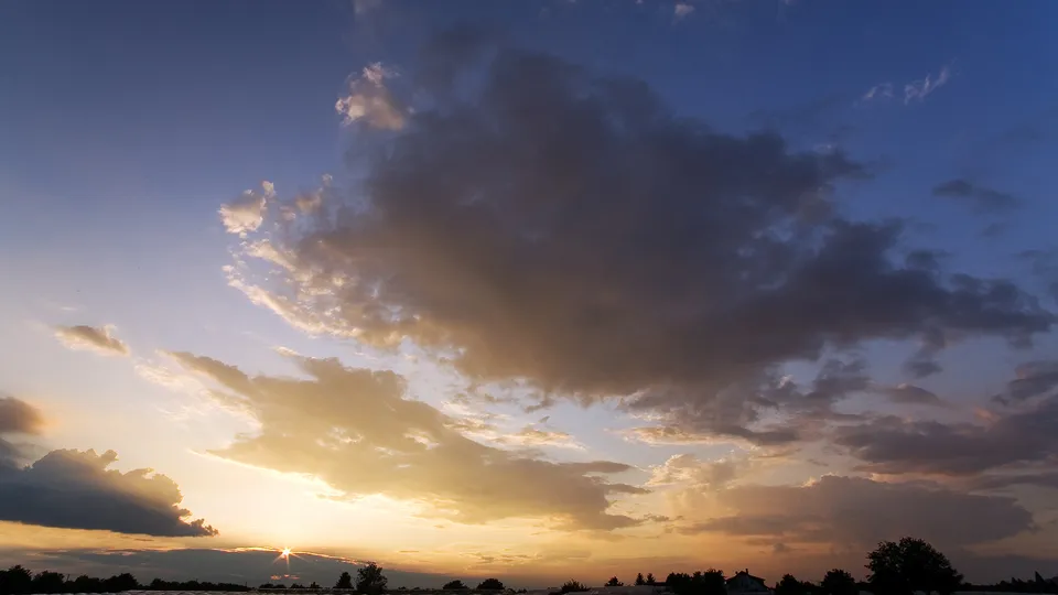 A dramatic sunset sky with dark clouds illuminated by golden light from the setting sun.