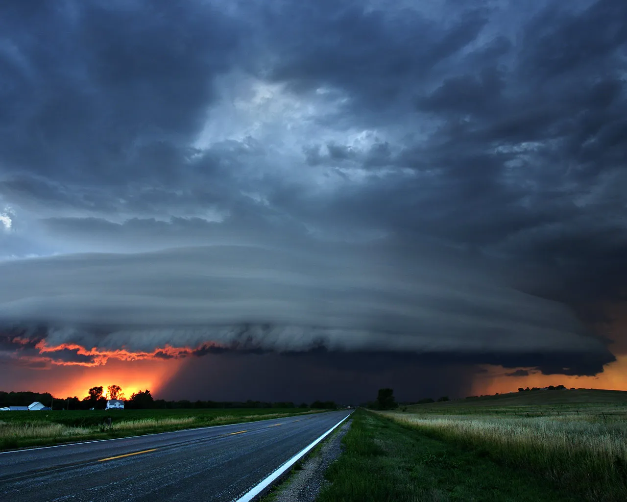 A supercell thunderstorm at sunset with vibrant orange light illuminating the clouds and landscape.