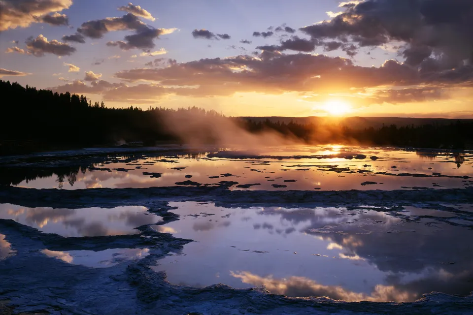 A sunset over a geothermal pool with steam rising and reflections in the water.