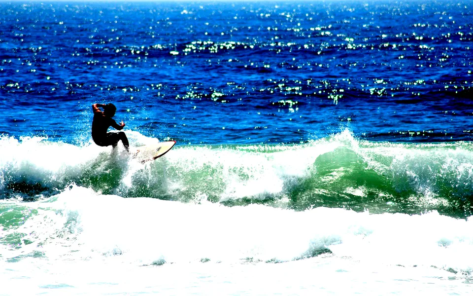 A surfer in silhouette rides a breaking wave with the deep blue ocean in the background.