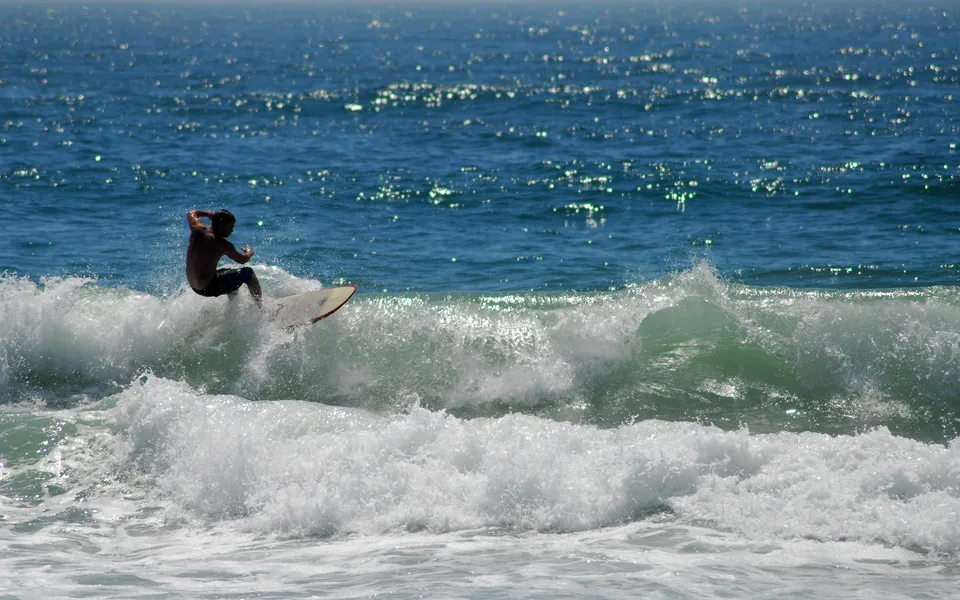 A surfer rides a wave with the blue ocean and sparkling water in the background.