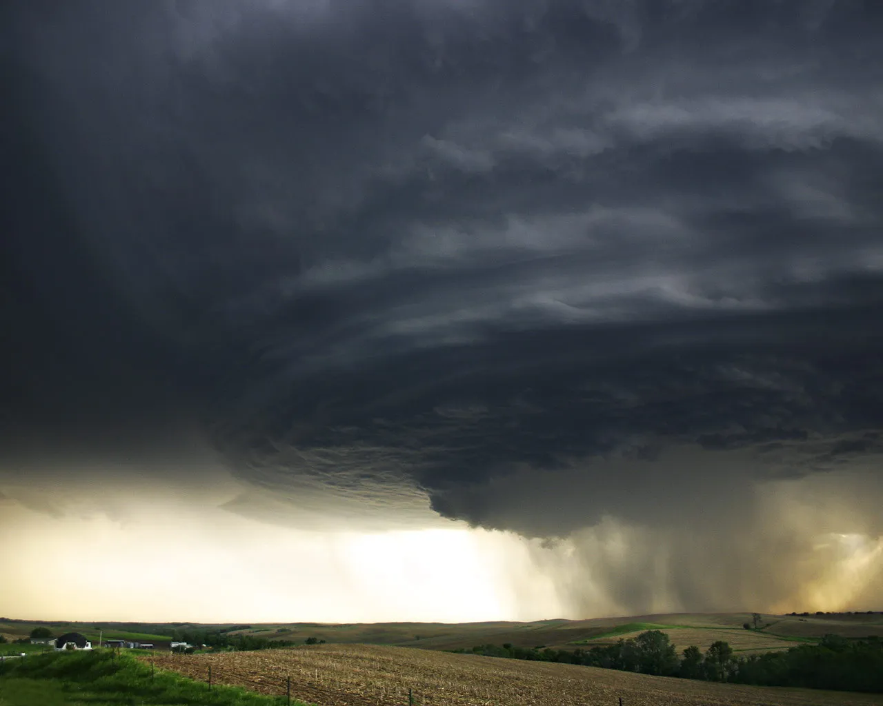 A powerful supercell thunderstorm with dark, swirling clouds and visible rain shafts.