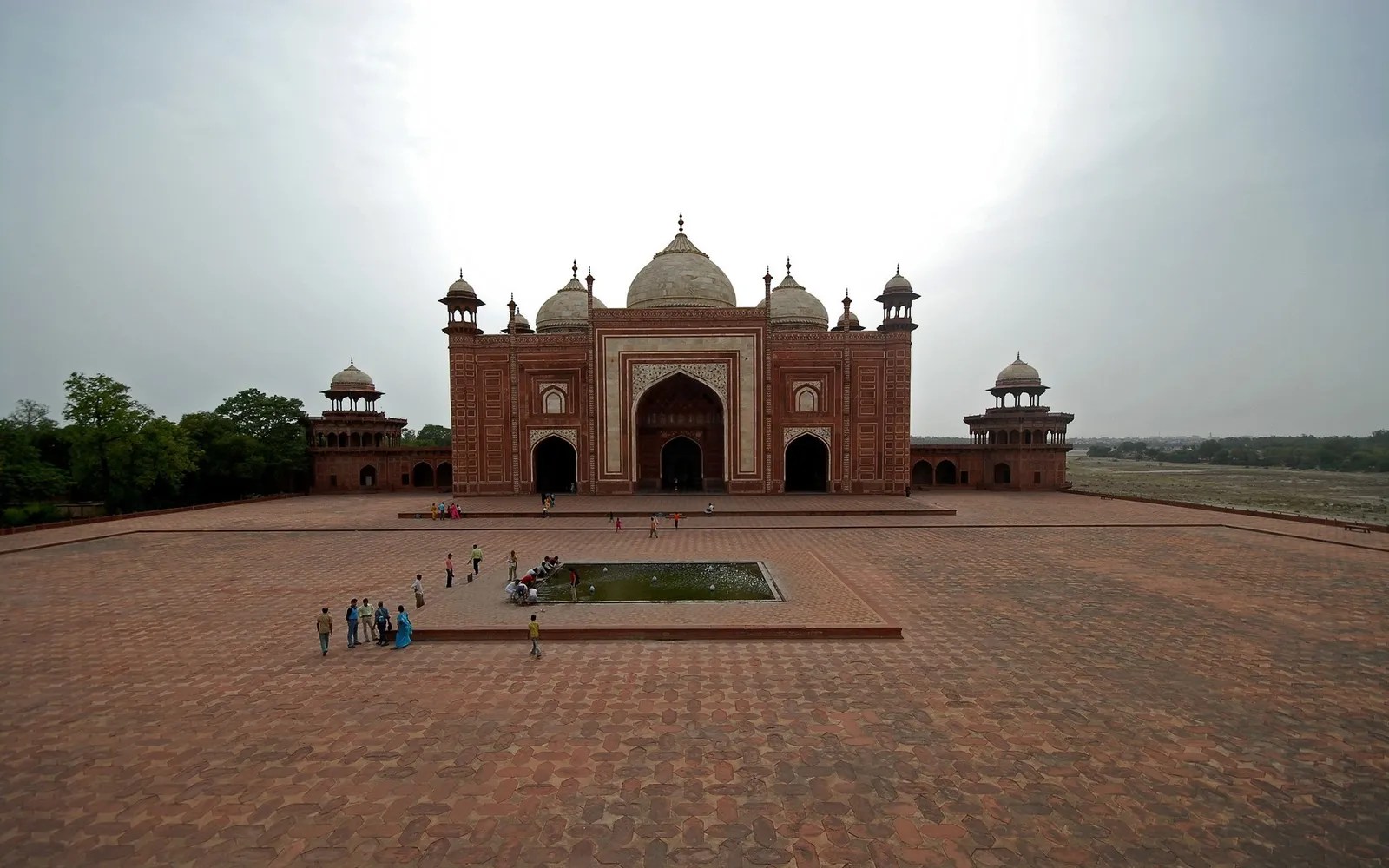 A wide view of the Taj Mahal complex with its red sandstone buildings and a reflecting pool.