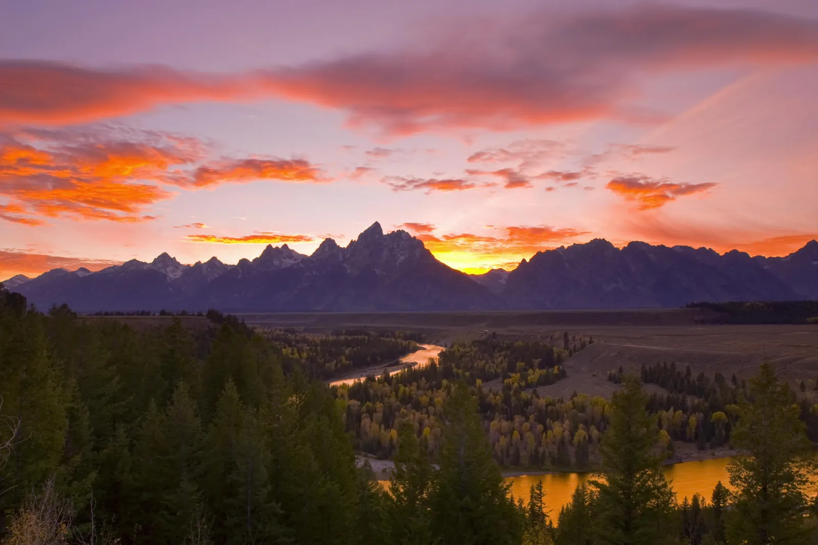 A vibrant sunset paints the sky with orange and pink hues over a majestic mountain range and a winding river.