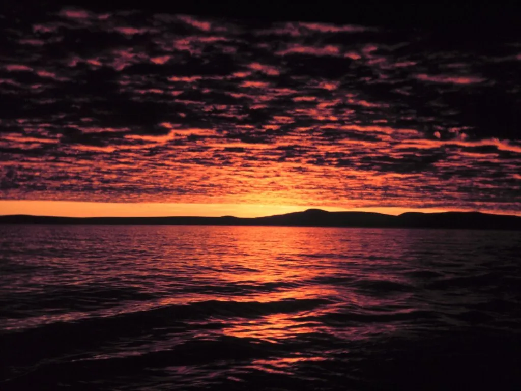 Dramatic orange and purple clouds fill the sky above a calm ocean at sunset.