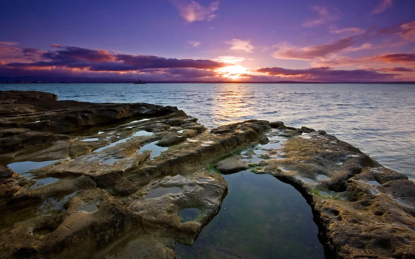 Textured rocks with tide pools reflecting the colorful sunset sky.