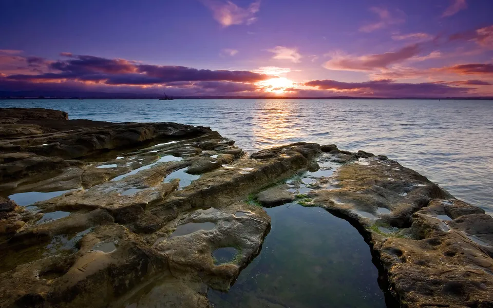 Textured rocks with tide pools reflecting the colorful sunset sky.