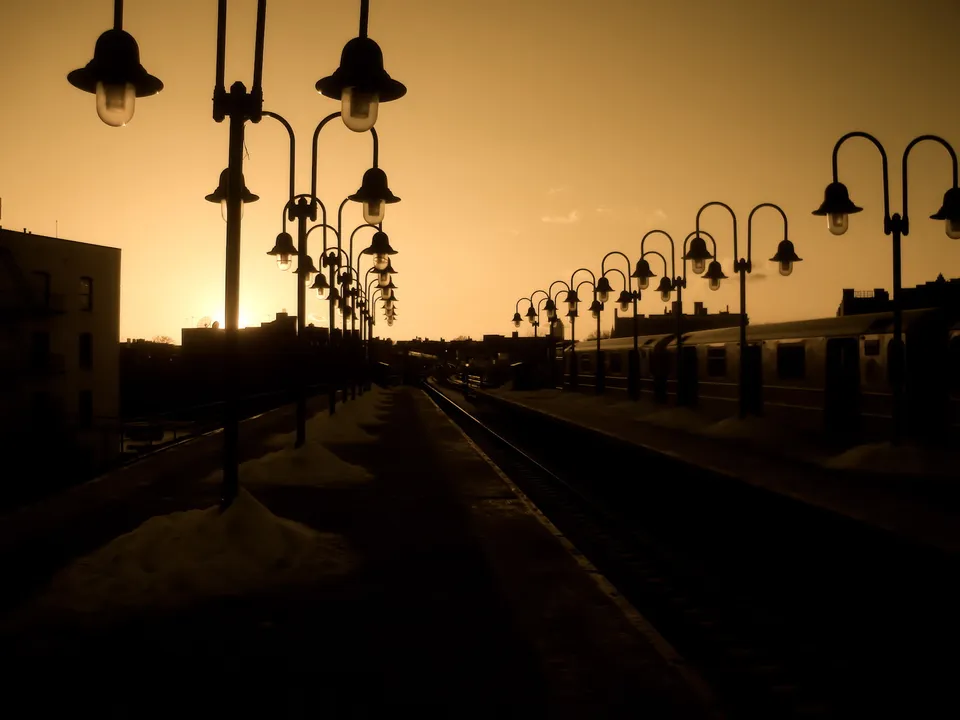 A row of vintage street lamps line a train platform at sunset with a train visible.