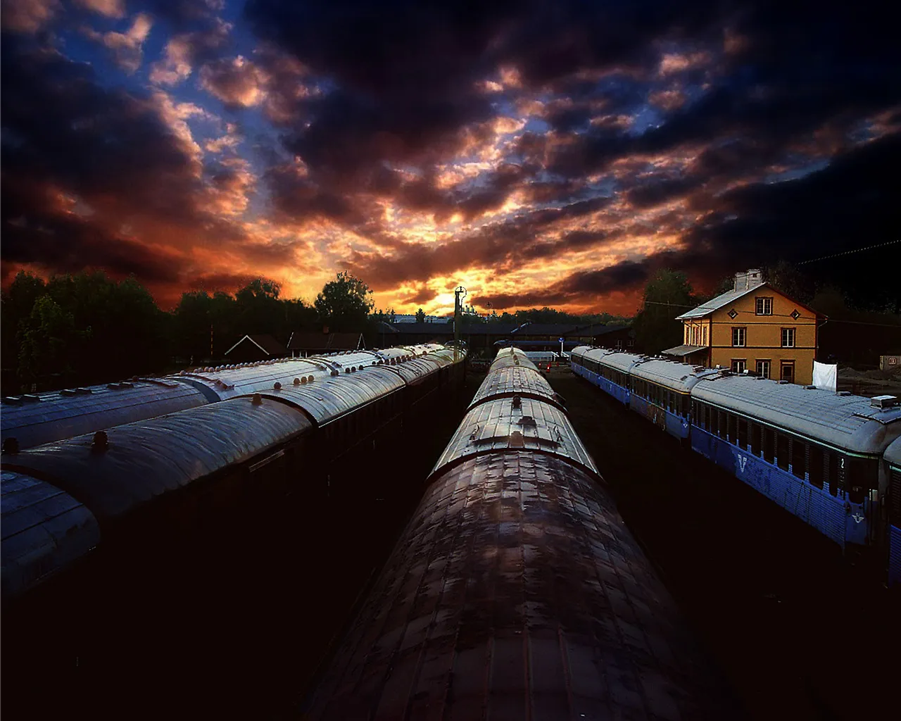 A dramatic sunset with fiery clouds over a train station with multiple train cars lined up.