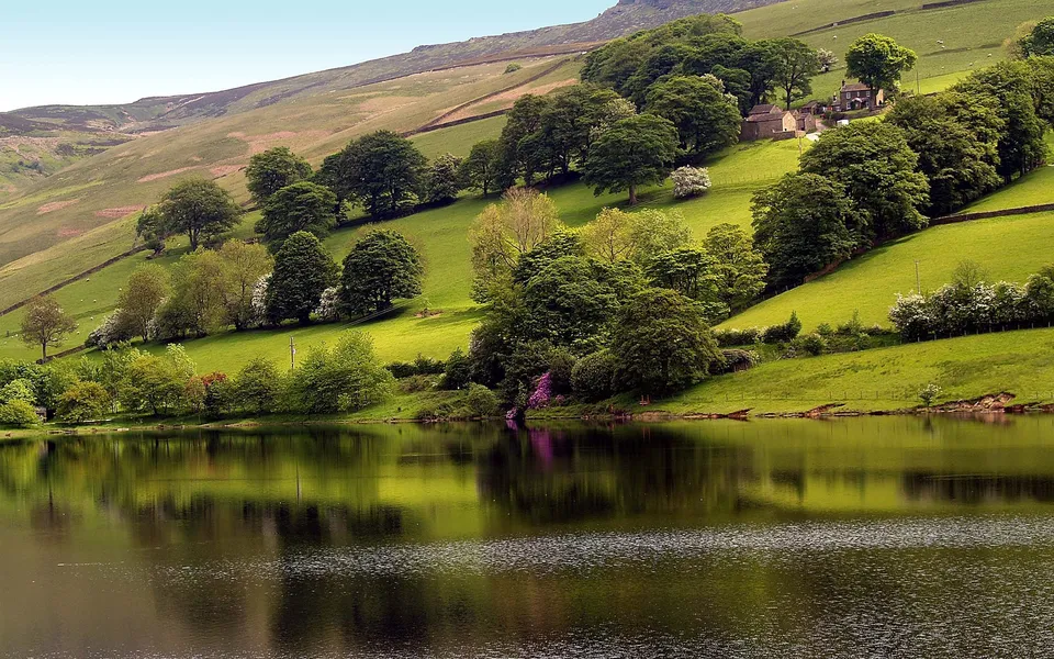 A calm lake reflects the lush green hills dotted with trees and a small village.