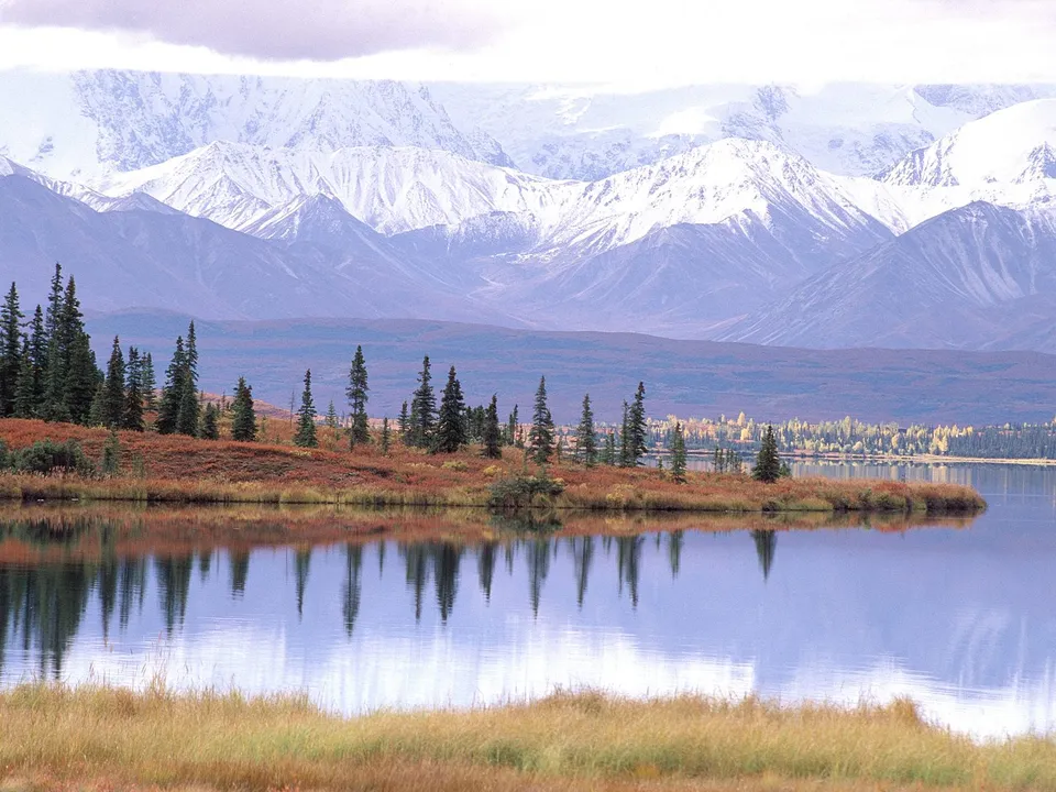 A tranquil lake mirrors snow-capped mountains and surrounding evergreen trees.