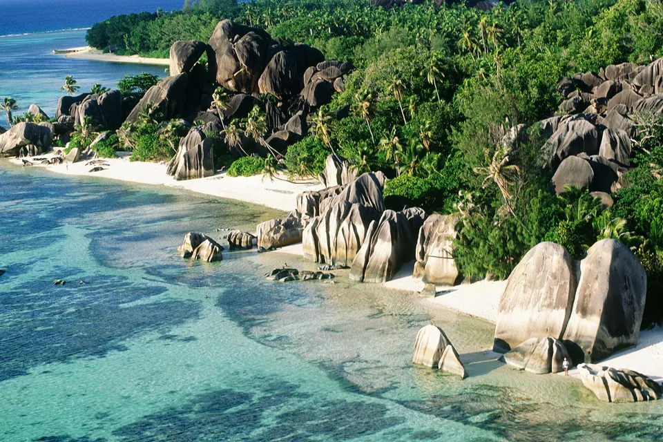 A tropical beach with large granite boulders, white sand, and clear turquoise water.