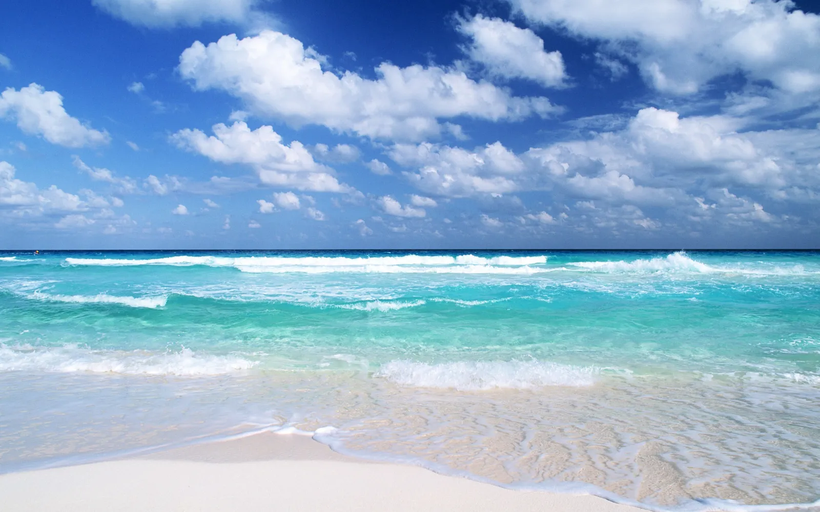 A beautiful tropical beach with clear turquoise water and white sand under a blue sky with fluffy clouds.