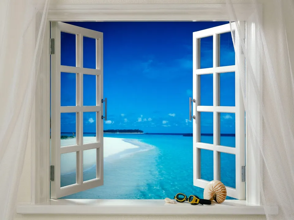 View of a tropical beach and ocean through an open window with a seashell and goggles on the sill.