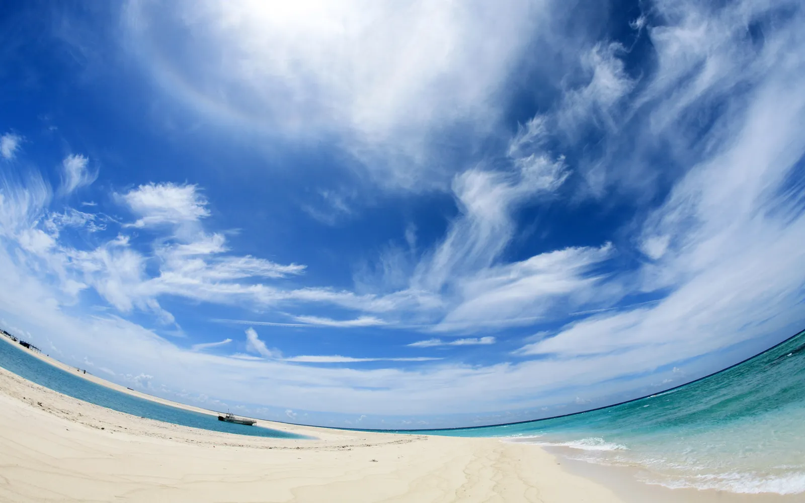 A wide sandy beach meets turquoise water under a bright blue sky with scattered wispy white clouds.
