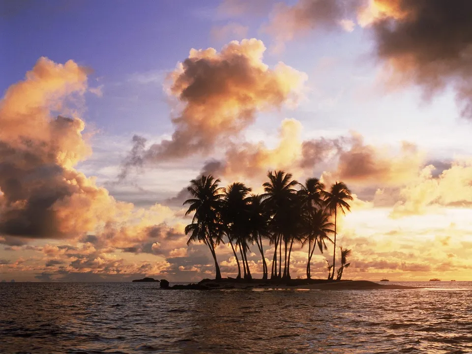 A small island with palm trees silhouetted against a dramatic sunset sky.