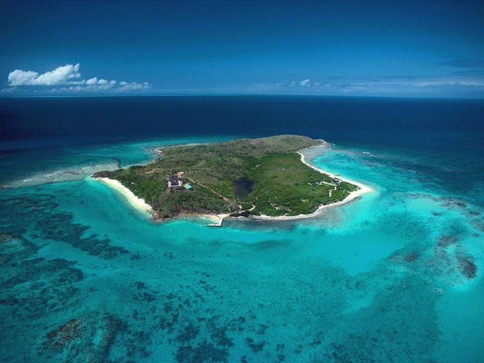 An aerial view of a lush green island surrounded by clear turquoise ocean water.