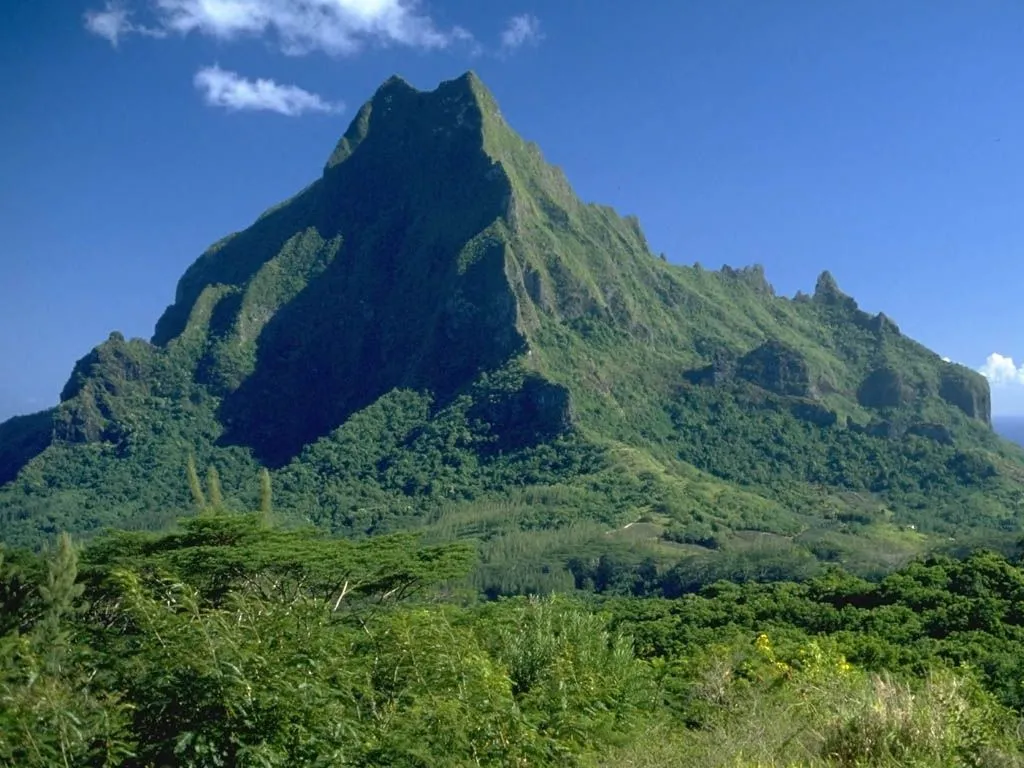 A majestic, verdant mountain peak rises under a clear blue sky with a few white clouds.