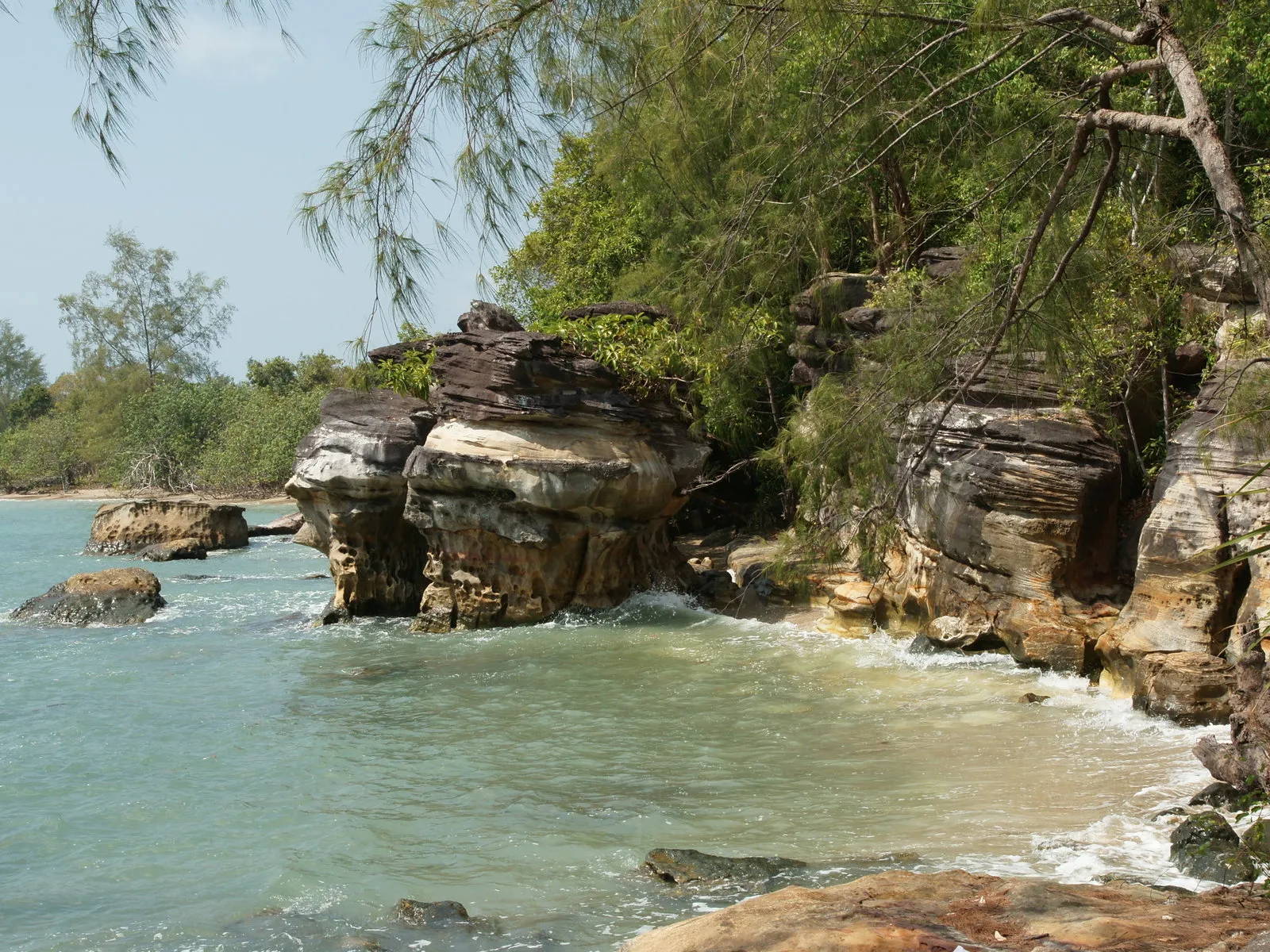 Waves gently lap against a rocky shoreline with lush green trees in the background.