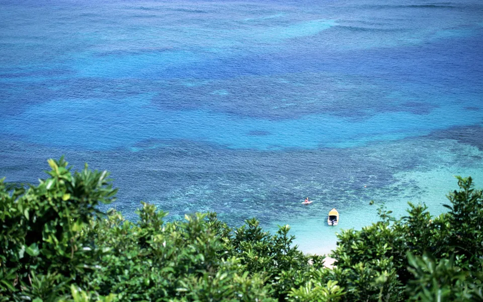 View from above of clear turquoise ocean water with a small boat and a kayaker.