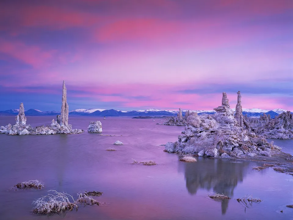 Tufa towers rise from a calm lake during a vibrant pink and purple sunset.
