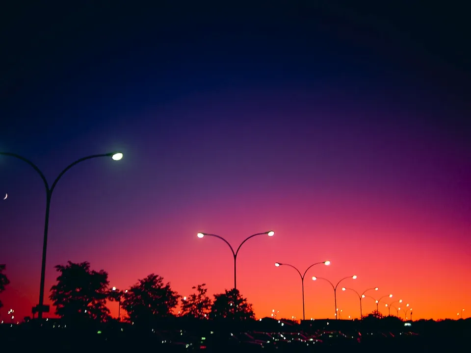 Streetlights and trees are silhouetted against a vibrant twilight gradient sky.