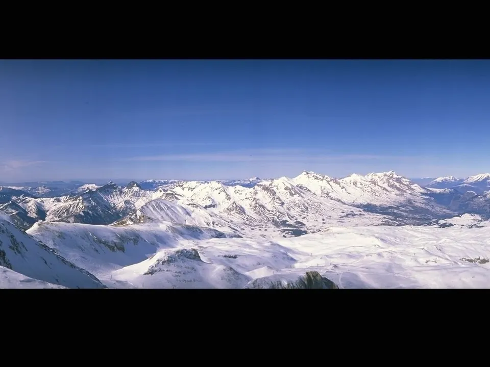 A panoramic view of a vast, snow-capped mountain range stretching across the horizon under a deep, clear blue sky.