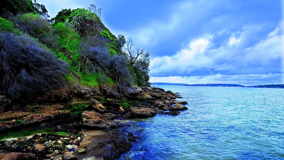 Rugged coastline with vegetated cliff and blue ocean under a dramatic cloudy sky.