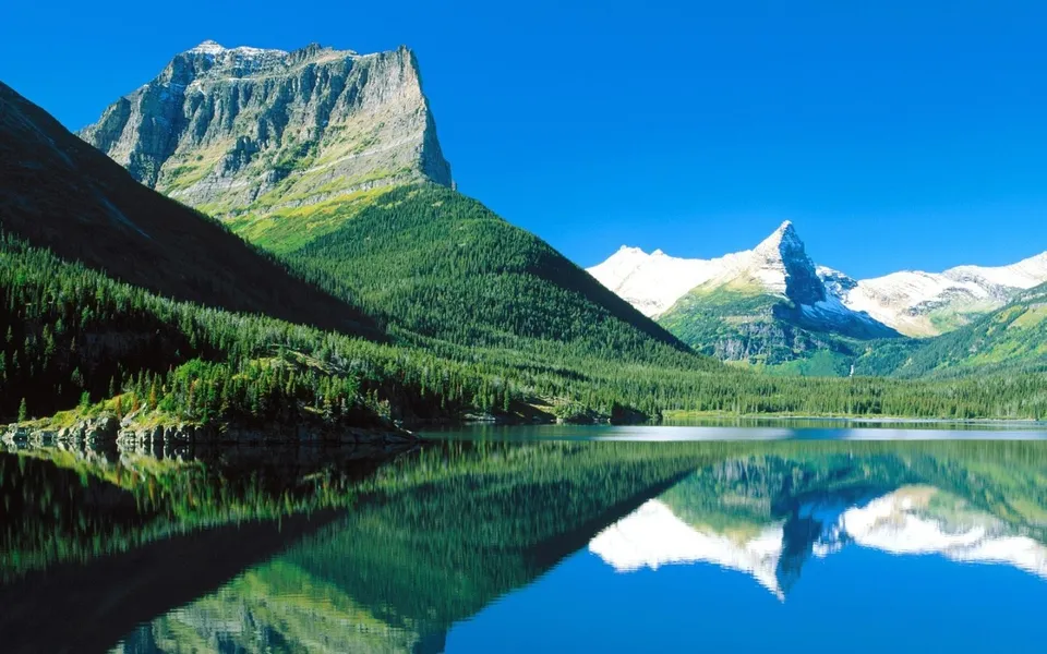 A clear blue sky reflects in a crystal-clear mountain lake.