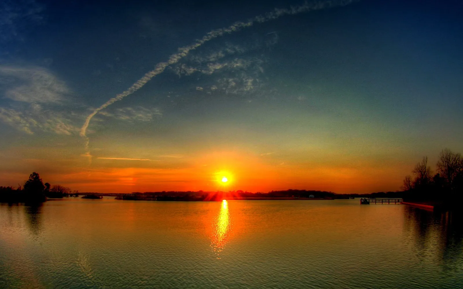 A vibrant orange and yellow sunset glows across the horizon of a wide, calm body of water.