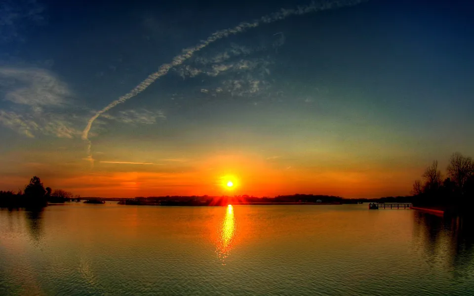 A vibrant orange and yellow sunset glows across the horizon of a wide, calm body of water.