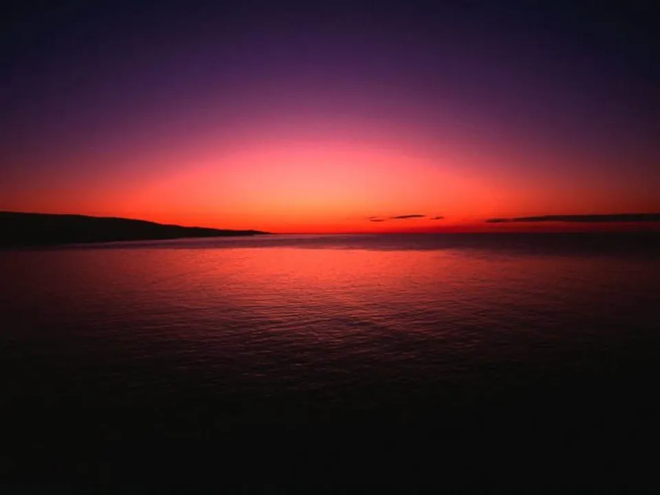 A dramatic sunset paints the sky with orange, pink, and purple hues above a calm ocean.