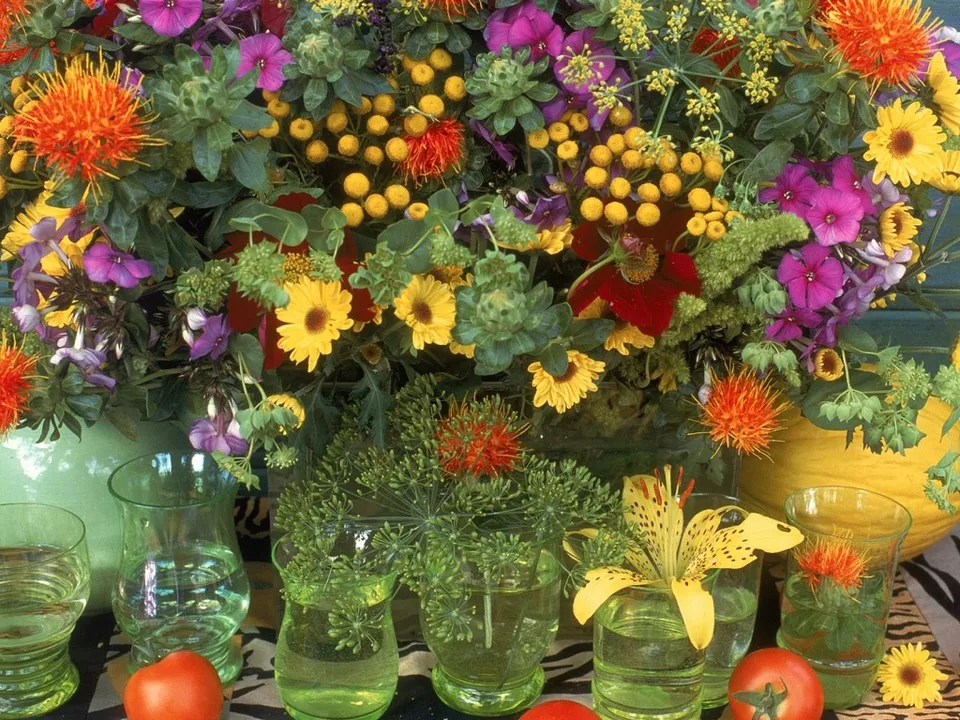 A colorful arrangement of various flowers and greenery in vases, with tomatoes in the foreground.